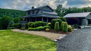 A two-story house with a porch, surrounded by well-maintained lawns and hedges. - Spacious mountain home 3mi south of Blowing Rock, NC, views, creek, 56 acres. (Lenoir)