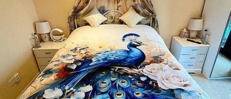 Een bed met een sprei met pauwenprint, een hemelbed en een nachtkastje met een lamp.