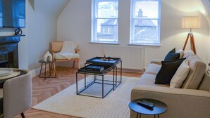 A living room with a sofa, armchair, coffee table, and a TV. There are two windows with blinds, a lamp, and a radiator. - The location for exploring York is fantastic. (York)