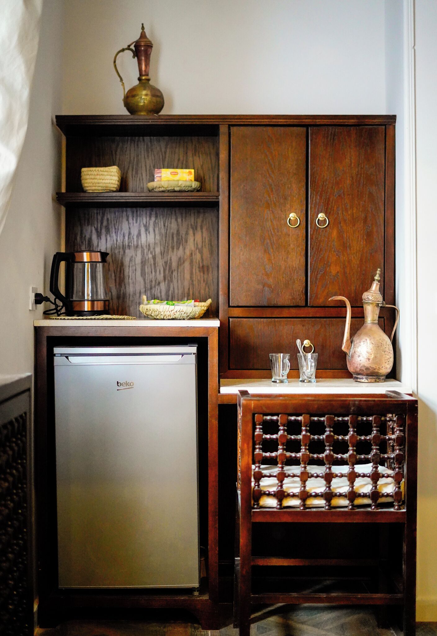 Una kitchenette compacta con refrigerador, cafetera, estante para especias y un armario de dos puertas.