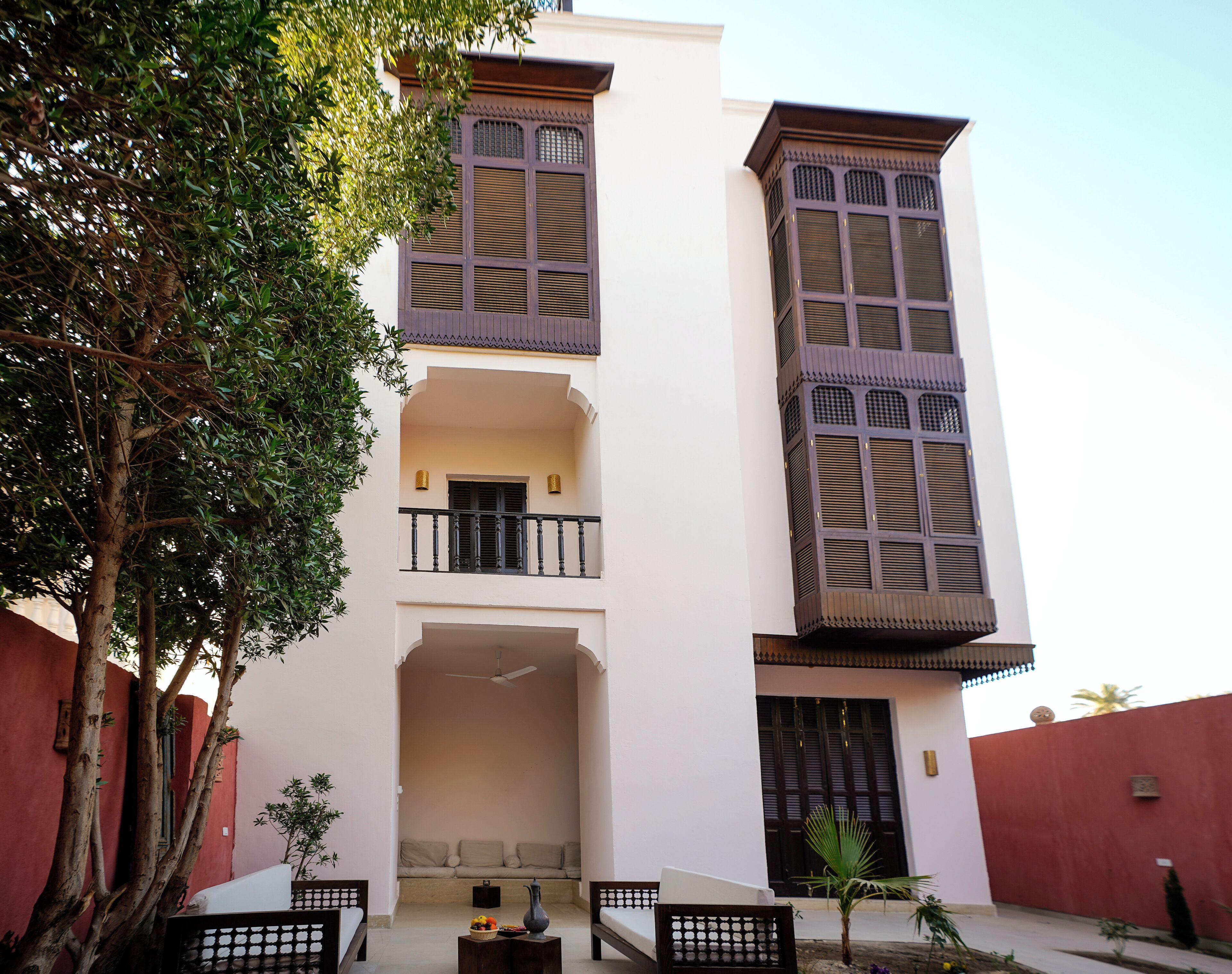 A multi-story building with balconies, a central courtyard, and a tree in the foreground.