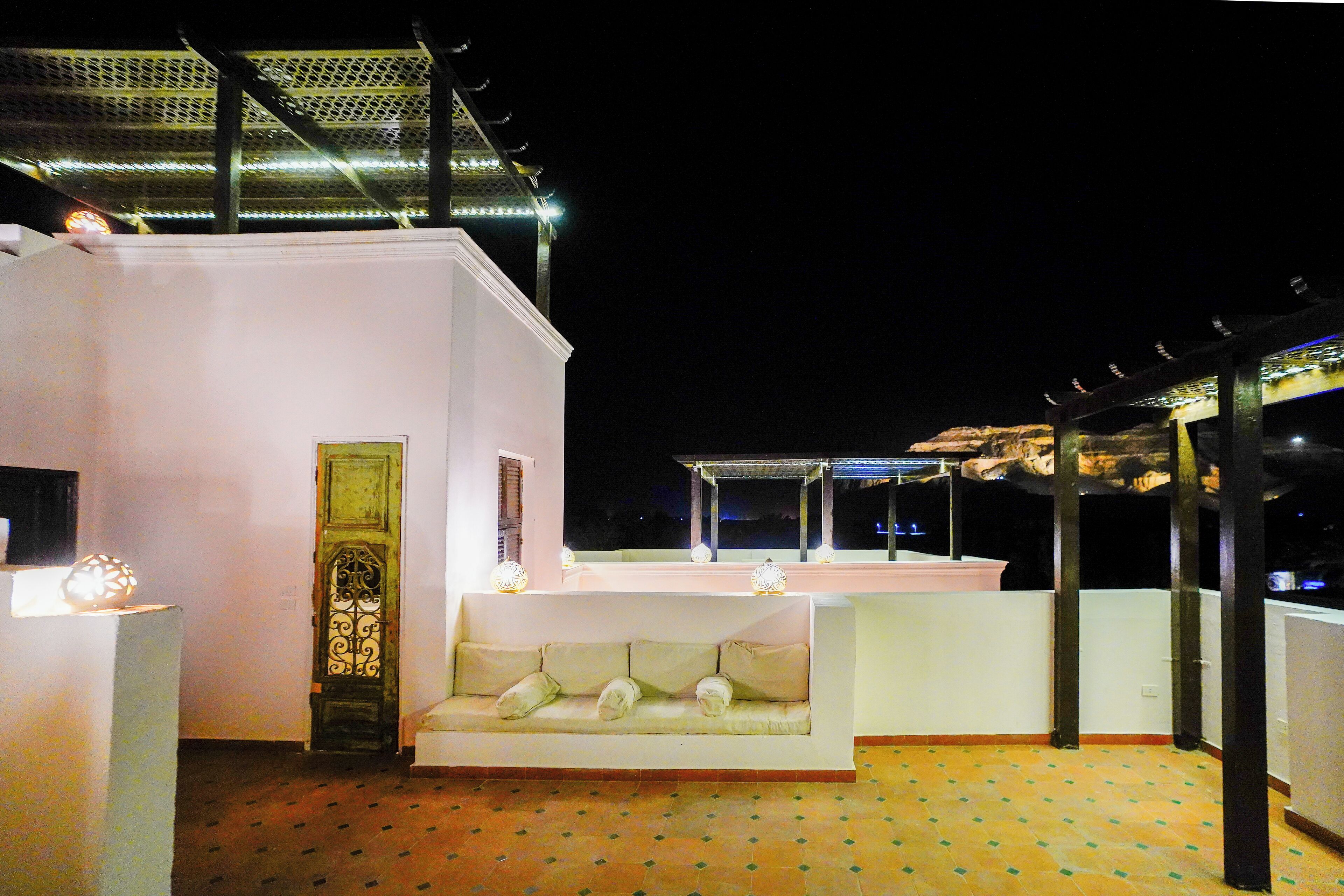 Eine Dachterrasse mit weißer Couch, einer Zierhaustür und einer Pergola.