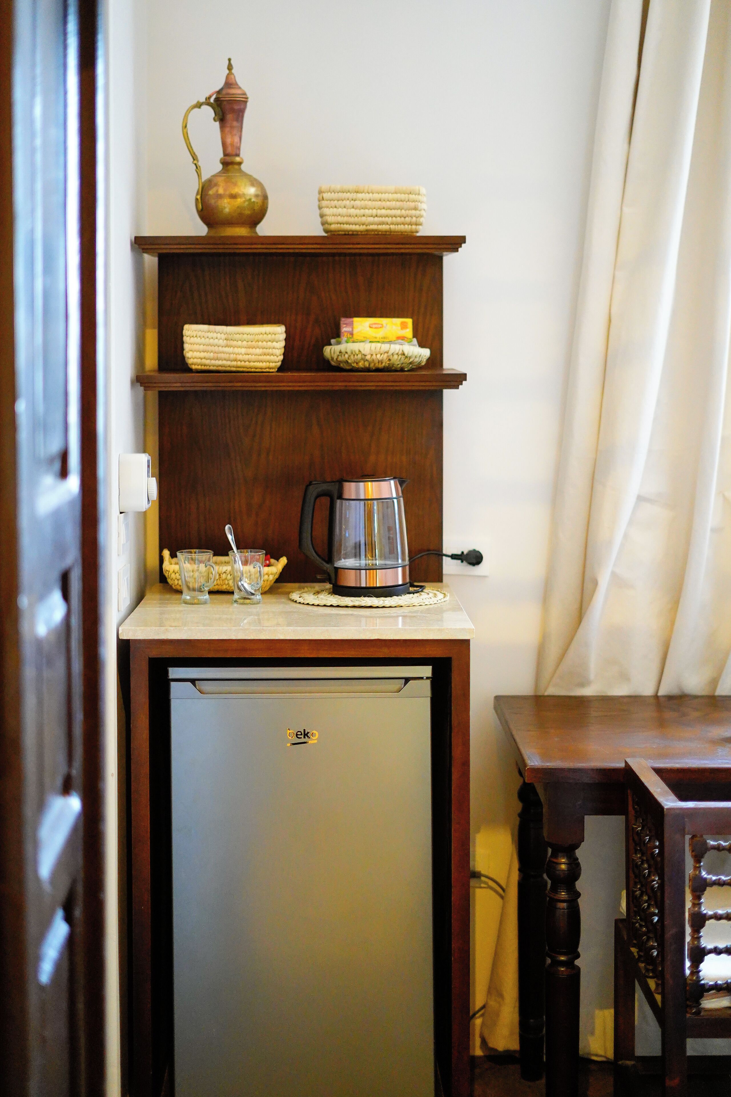 A compact kitchen area with a refrigerator, a coffee maker, and a shelf with bowls and a vase.