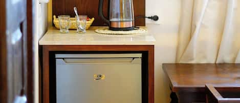 A compact kitchen area with a refrigerator, a coffee maker, and a shelf with bowls and a vase.