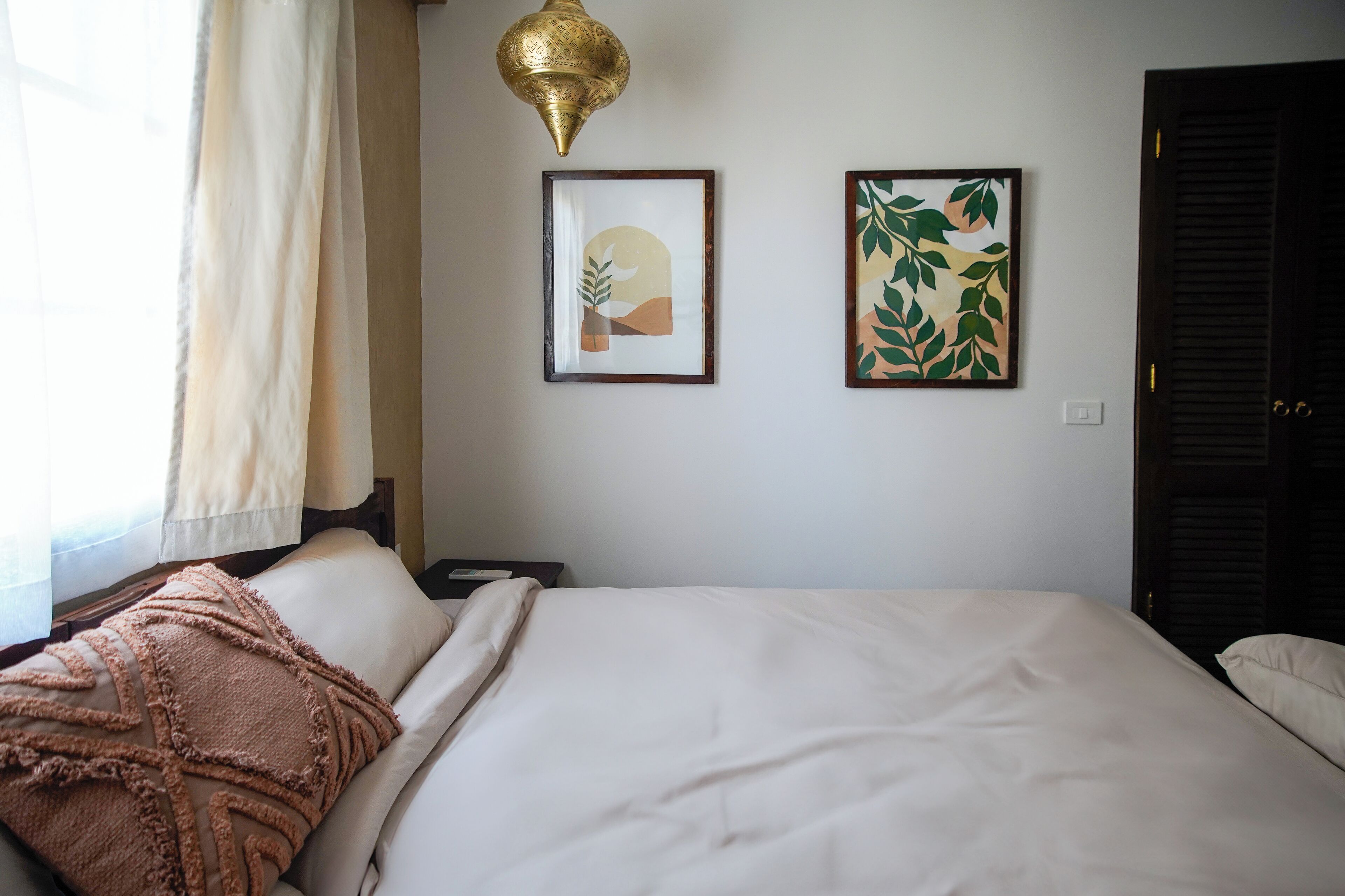 Ein Hotelzimmer mit einem Bett, einem Nachttisch, einer Lampe und zwei gerahmten Bildern an der Wand.