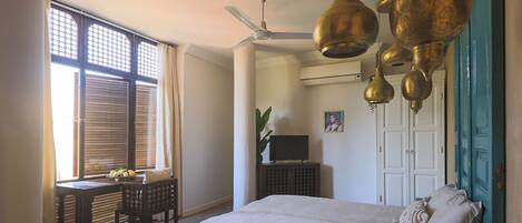 A bedroom with a bed, a desk with a chair, a television, and a ceiling fan.