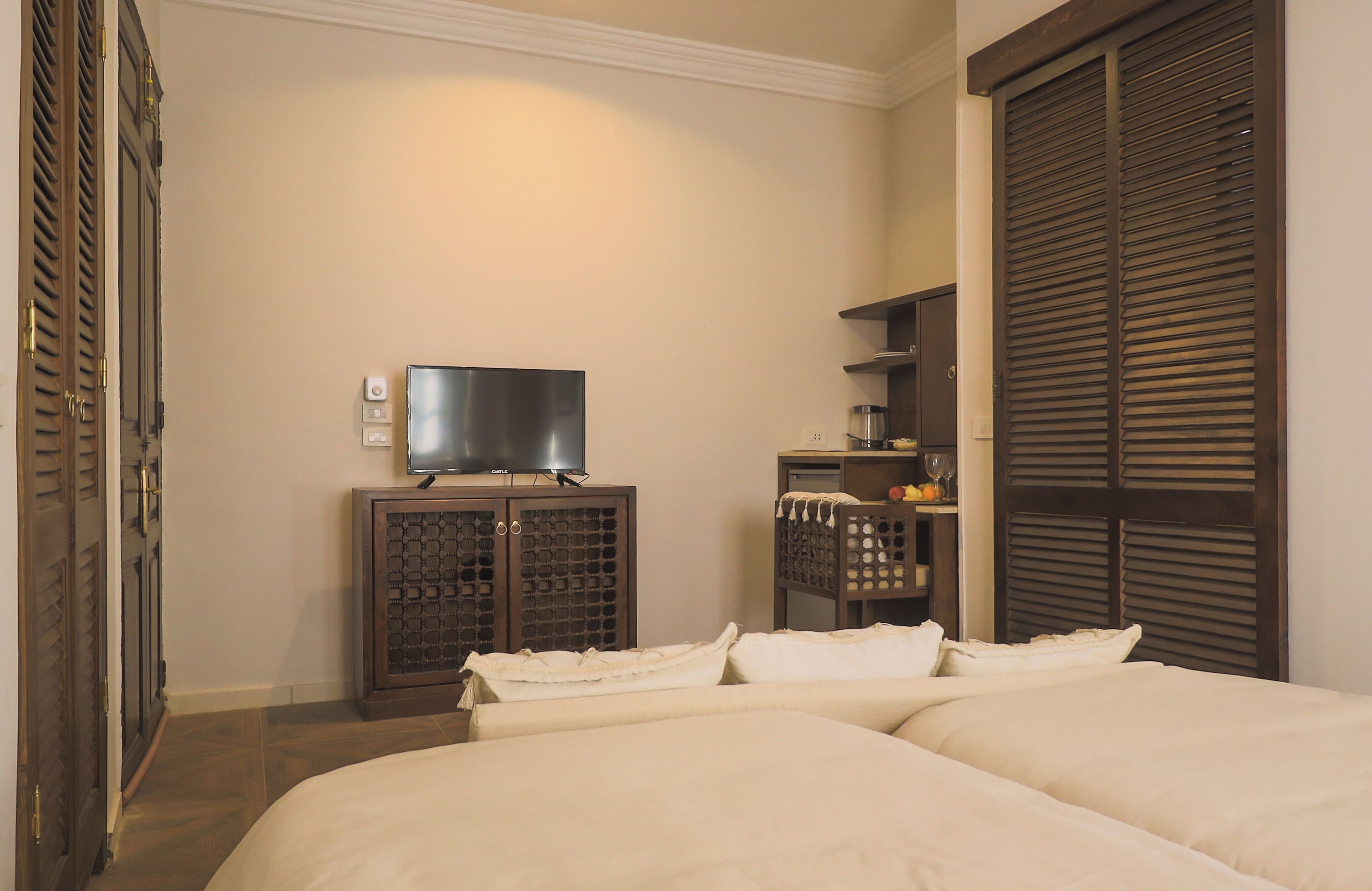 A hotel room with a bed, a television on a cabinet, a wine rack, and a wardrobe with louvered doors.