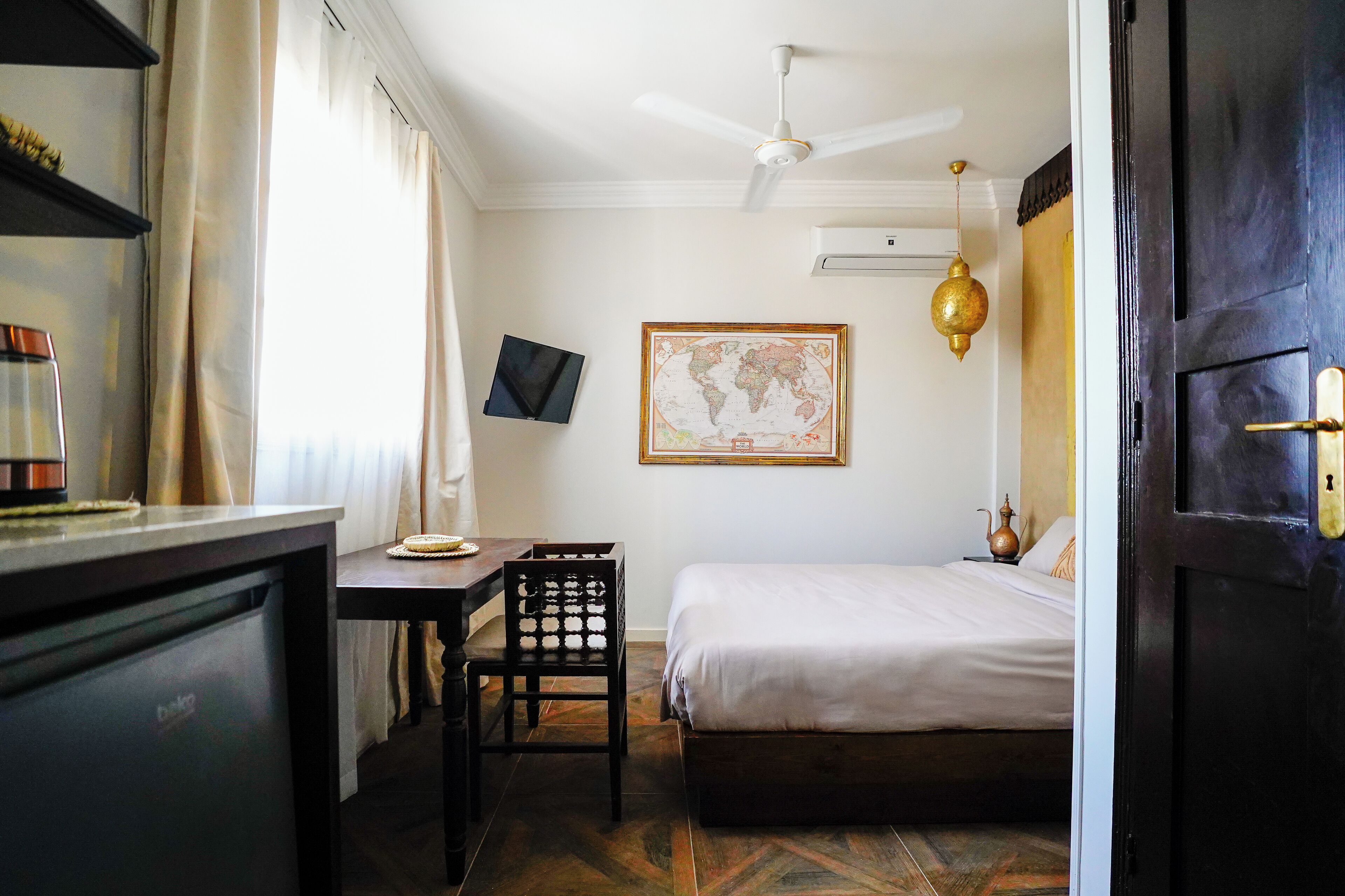 Un dormitorio con cama, escritorio, silla, mapa en la pared y ventilador de techo.