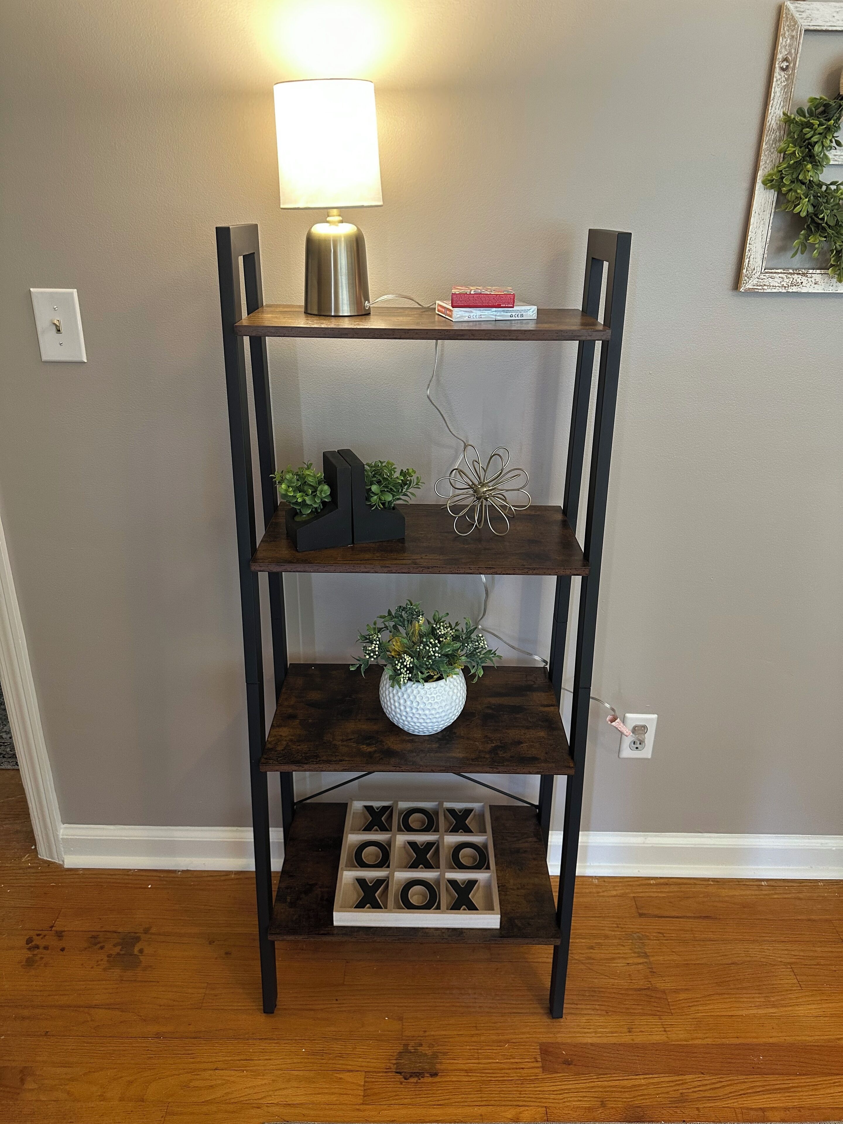 A wooden multi-tiered shelf with a lamp, plants, and a wooden block puzzle.