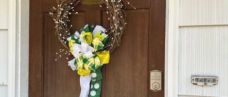 A wooden door with a wreath and a yellow and white bow.