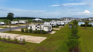 A campground with RVs parked in rows, a paved road, and a body of water in the background. -  RV Lot 67 in Grand Riviera Resort in Foley, AL. Daily and long term available (Foley)