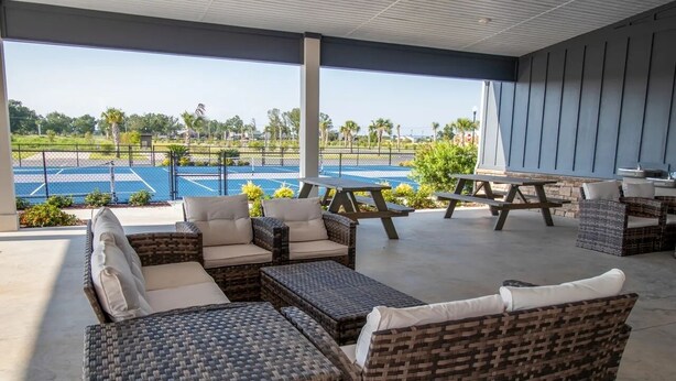 A covered outdoor seating area with wicker furniture and a view of a tennis court. -  RV Lot 67 in Grand Riviera Resort in Foley, AL. Daily and long term available (Foley)