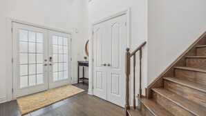 Un couloir avec deux portes blanches, un escalier en bois et une petite table sur laquelle est posée une plante.
