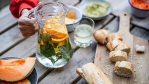 A pitcher filled with a beverage, slices of orange, and mint leaves on a wooden table.