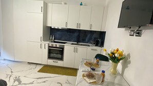 A compact kitchen with white cabinets, a built-in oven, and a dining area with a table set for two. - Promotion - Fully Equipped Studio for Short and Long Stays in Legnano (Legnano)