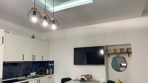 A modern kitchen with white cabinets, a black stove, and a dining area with a white table and two green chairs. - Promotion - Fully Equipped Studio for Short and Long Stays in Legnano (Legnano)