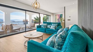 A spacious living room with a teal sofa, a round coffee table, and a balcony with a view of the sea. - Casa Hurlavente | Luxury Villa on Punta de Mona | 4 En-suite Bedrooms | Heated Private Pool | Panoramic Sea Views | Roof Terrace (La Herradura)