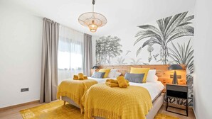 A bedroom with two beds, a wooden headboard, a yellow throw blanket, a woven rug, and a wall mural of tropical plants. - Casa Hurlavente | Luxury Villa on Punta de Mona | 4 En-suite Bedrooms | Heated Private Pool | Panoramic Sea Views | Roof Terrace (La Herradura)