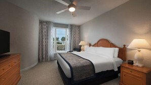 A hotel room with a bed, two bedside tables with lamps, a ceiling fan, a window with curtains, and a TV on a dresser. - Monarch at Sea Pines, 2-bedroom condo in Hilton Head Island, WiFi, fitness room (Hilton Head Island)