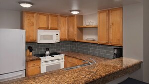 A kitchen with wooden cabinets, a white microwave, a stove, and granite countertops. - Monarch at Sea Pines, 2-bedroom condo in Hilton Head Island, WiFi, fitness room (Hilton Head Island)