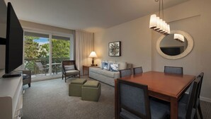 A hotel room with a dining table, chairs, a sofa, a TV, a lamp, a mirror, and a balcony with a view of trees. - Monarch at Sea Pines, 2-bedroom condo in Hilton Head Island, WiFi, fitness room (Hilton Head Island)
