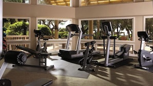 A gym with various exercise equipment, large windows with a view of greenery, and a wooden ceiling. - Monarch at Sea Pines, 2-bedroom condo in Hilton Head Island, WiFi, fitness room (Hilton Head Island)