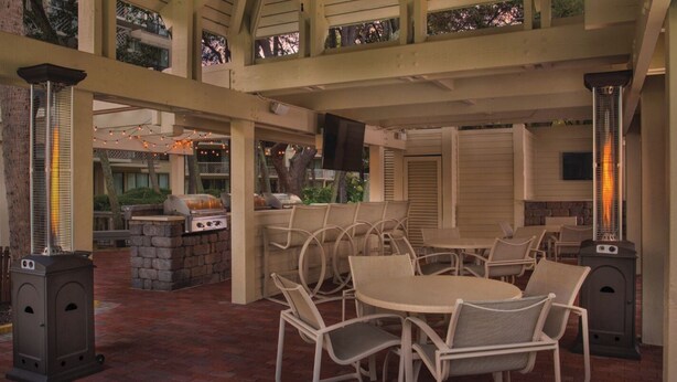An outdoor patio with a round table and chairs, a grill, and a stone fireplace. - Monarch at Sea Pines, 2-bedroom condo in Hilton Head Island, WiFi, fitness room (Hilton Head Island)