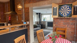 Een keuken met een dartbord, een eettafel met geruit tafelkleed en een open haard op de achtergrond.