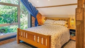 Een slaapkamer met een houten bed, een raam met gordijnen, een bakstenen muur en een nachtkastje met een lamp.