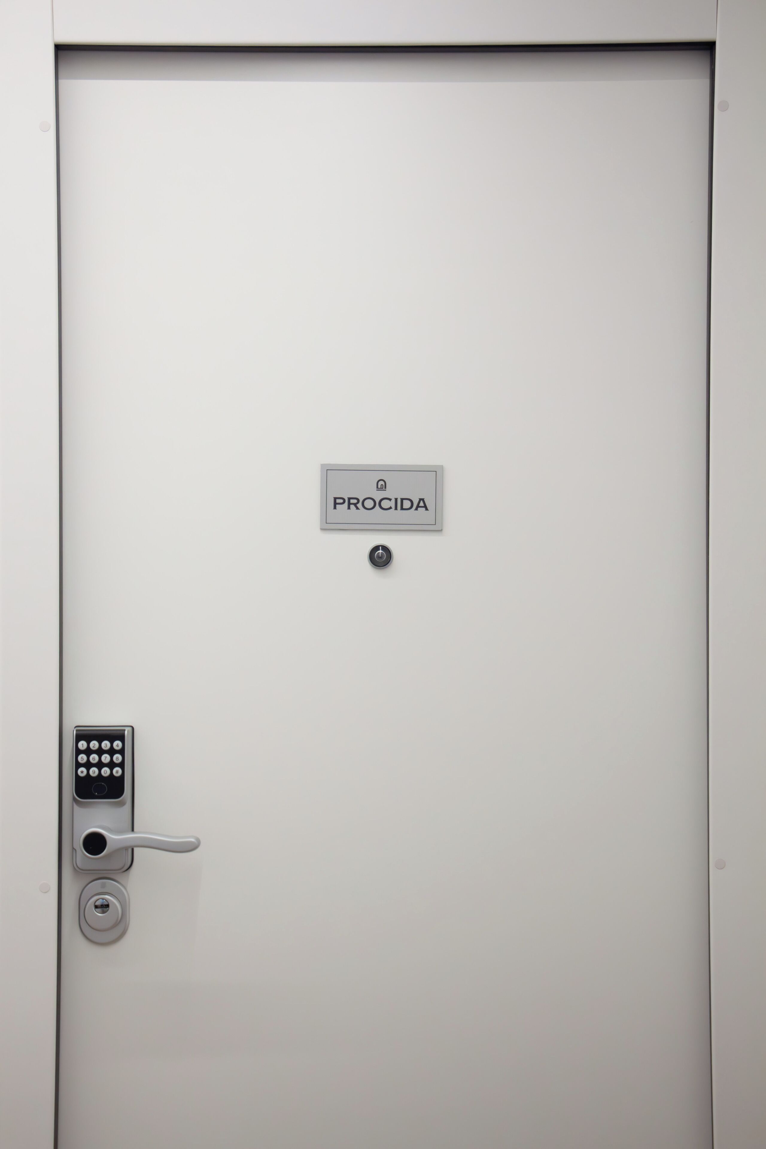 Una porta blanca amb un tancatiri numèric, un ull de claus i un senyal que diu "PROCIDA".