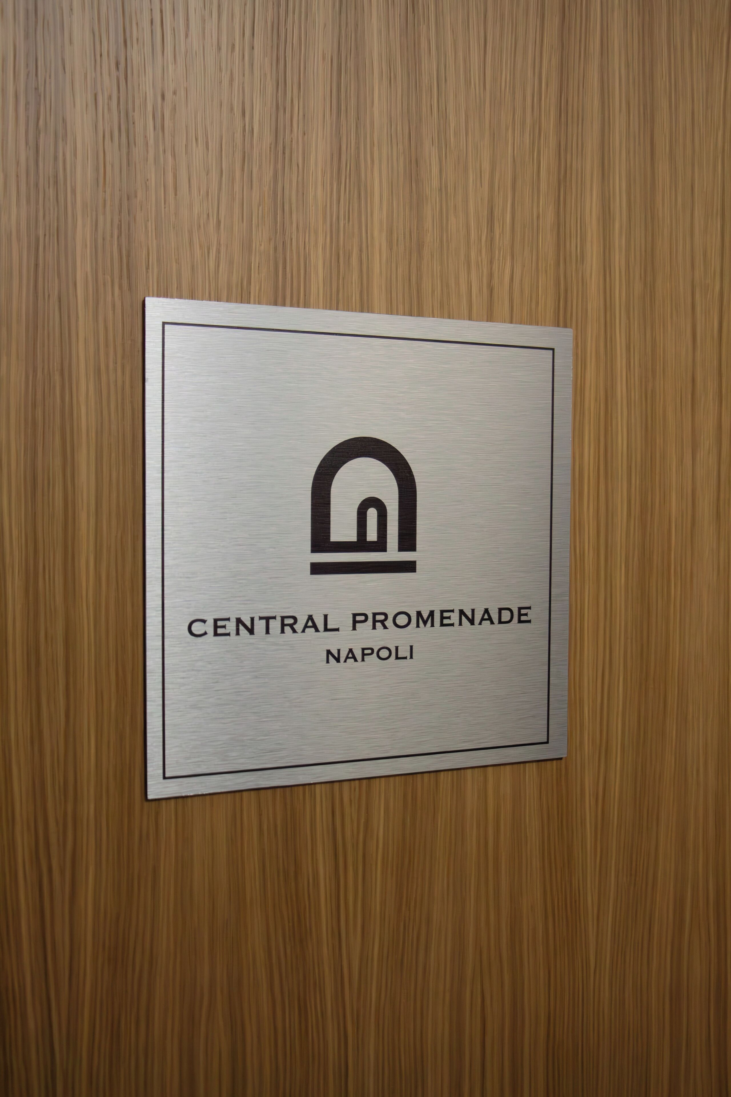 A sign with the text "CENTRAL PROMENADE NAPOLI" on a wooden door.