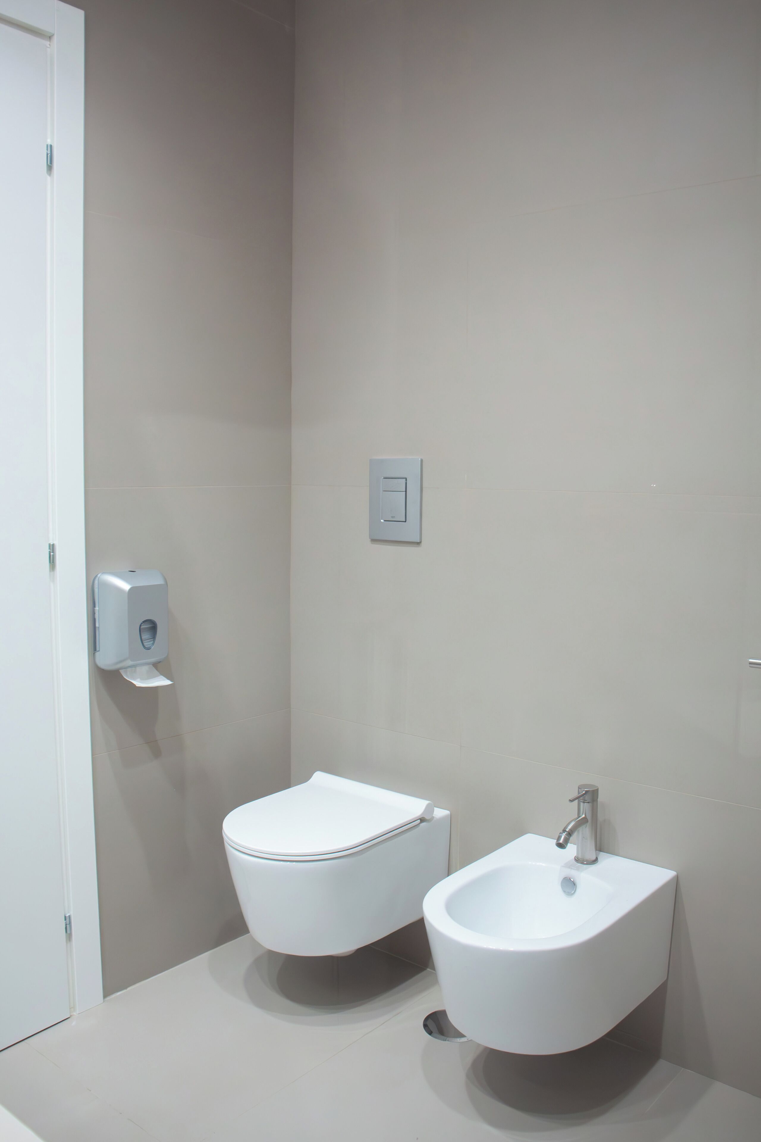 Un baño moderno con inodoro y bidé, un secador de manos y un interruptor de luz en la pared.