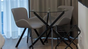 Une pièce moderne avec une table en verre, deux chaises, une chaise en métal noir et un tapis gris.
