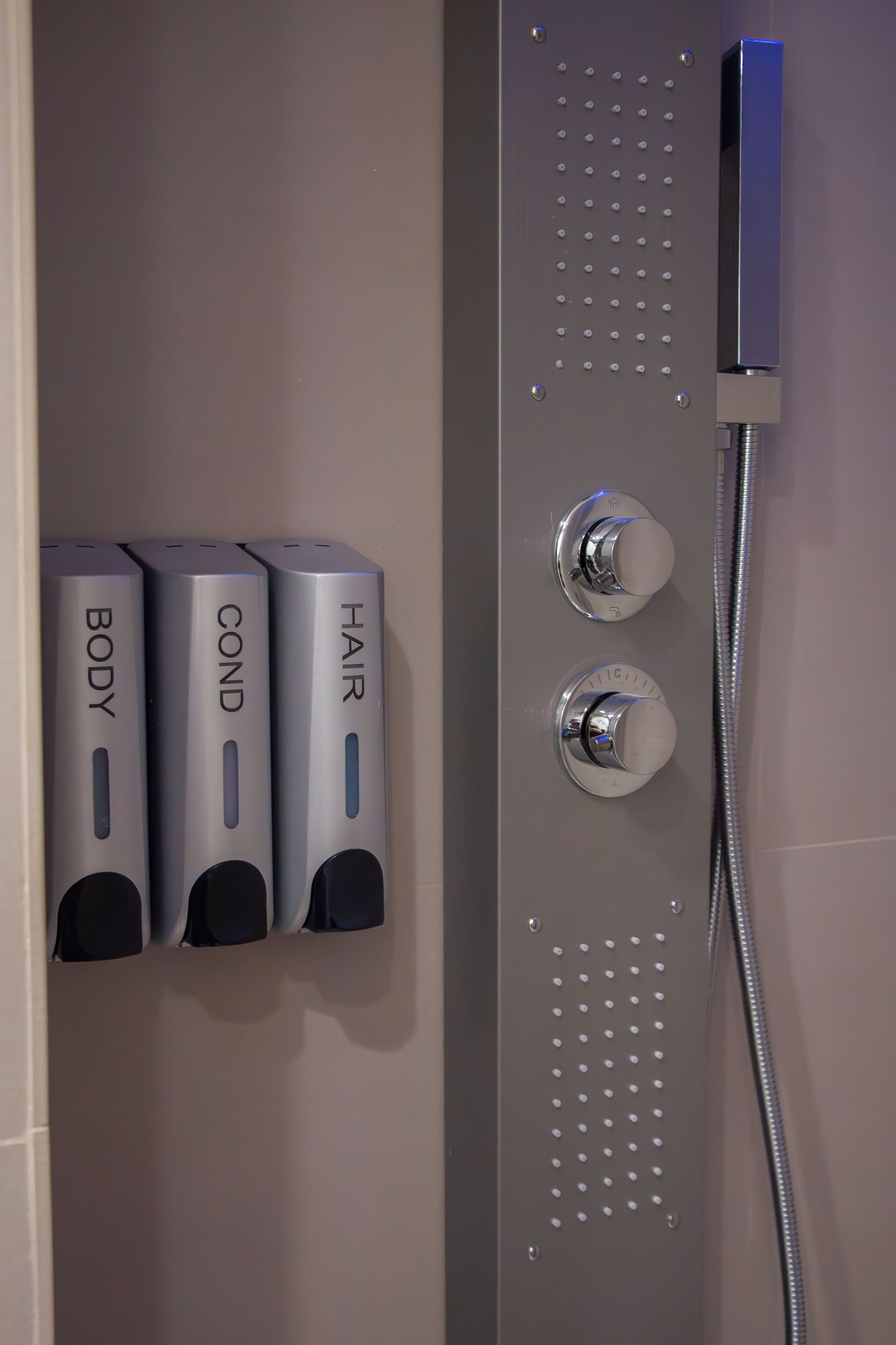Une salle de bain équipée de trois distributeurs de savon étiquetés « CORPS », « CHEVEUX » et « REVITALISANT ».