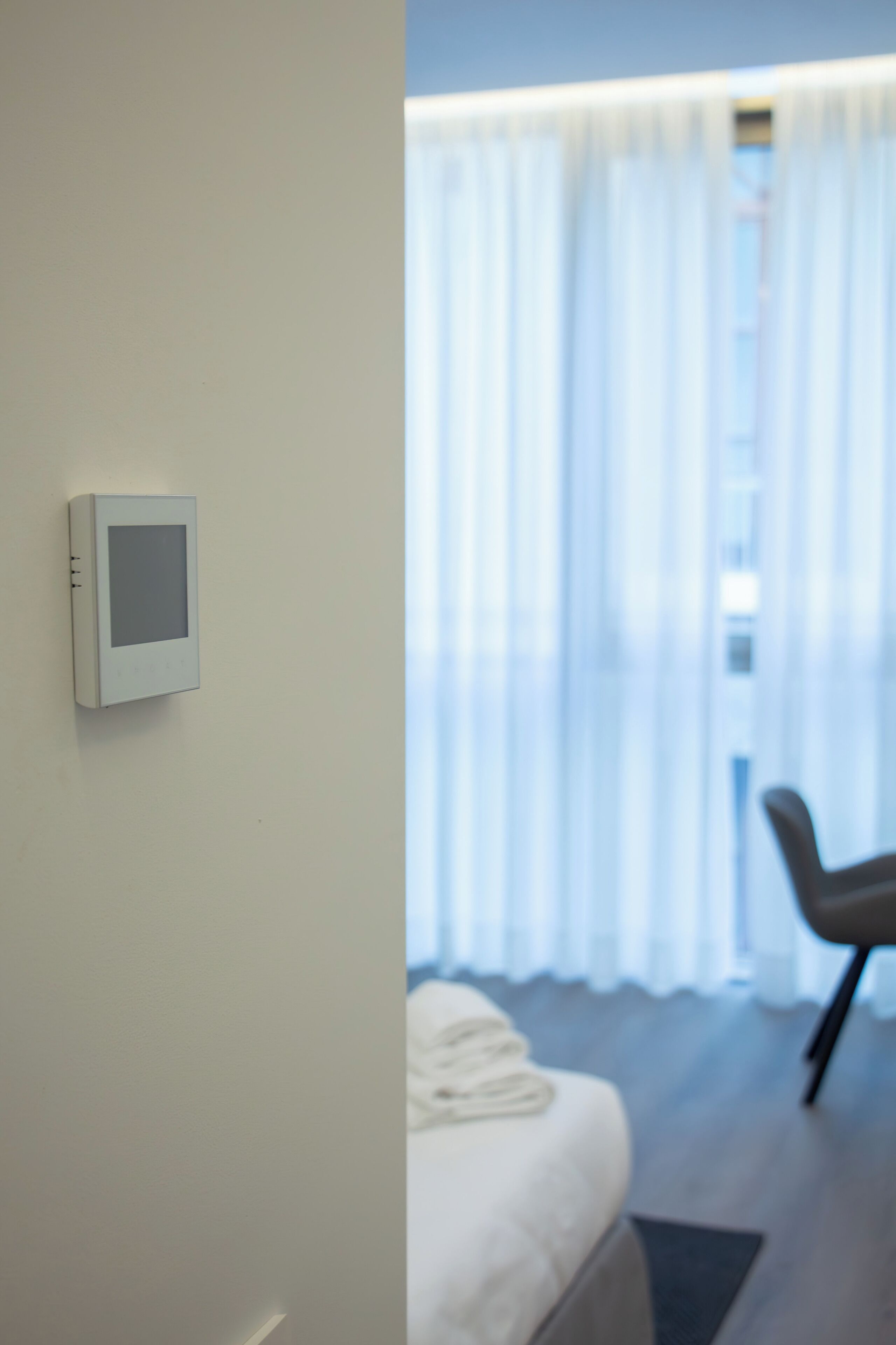 Une chambre d’hôtel avec un lit, une chaise et un panneau de commande fixé au mur.