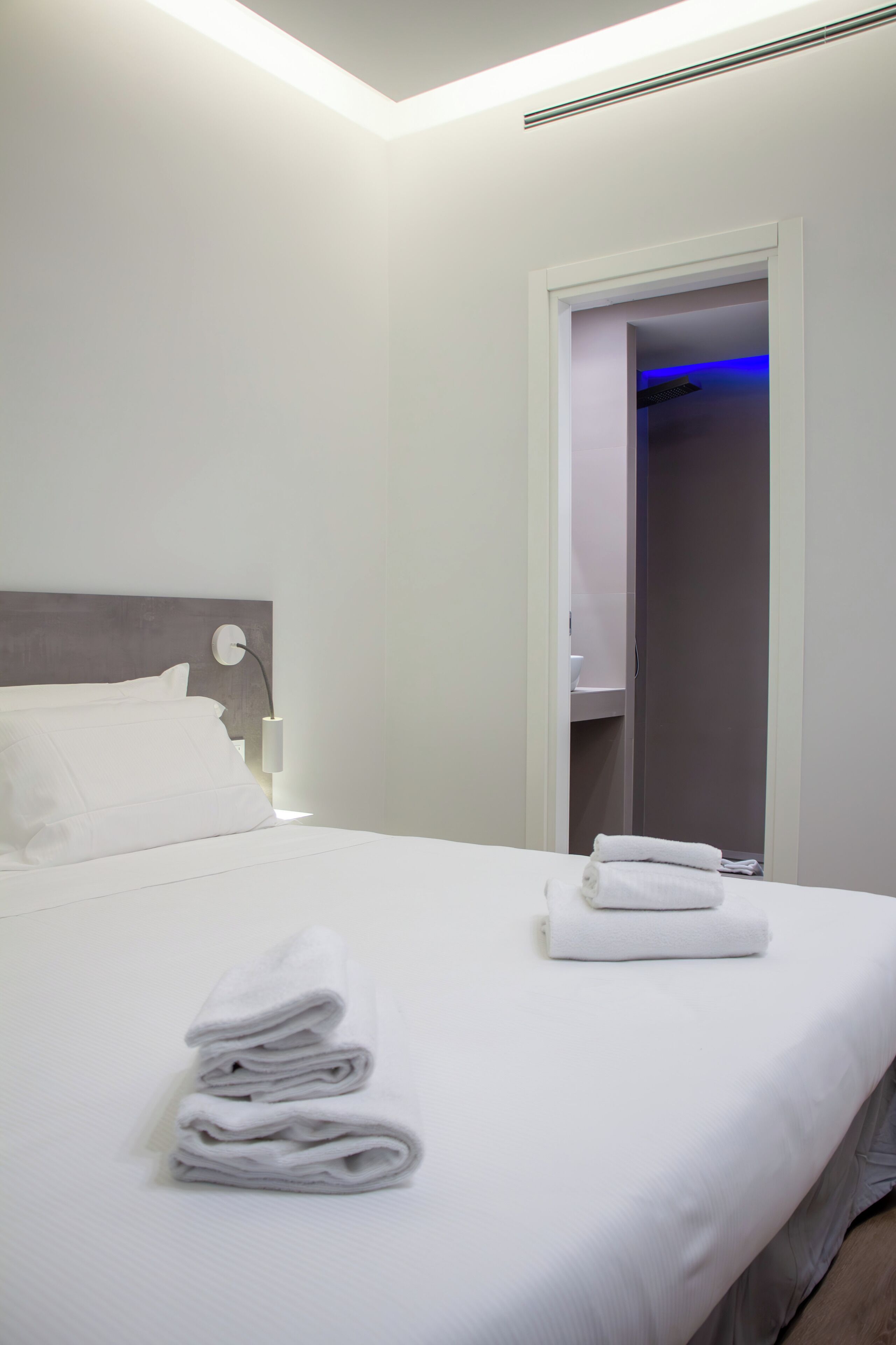 A neatly made bed with white linens and a folded towel on the side.