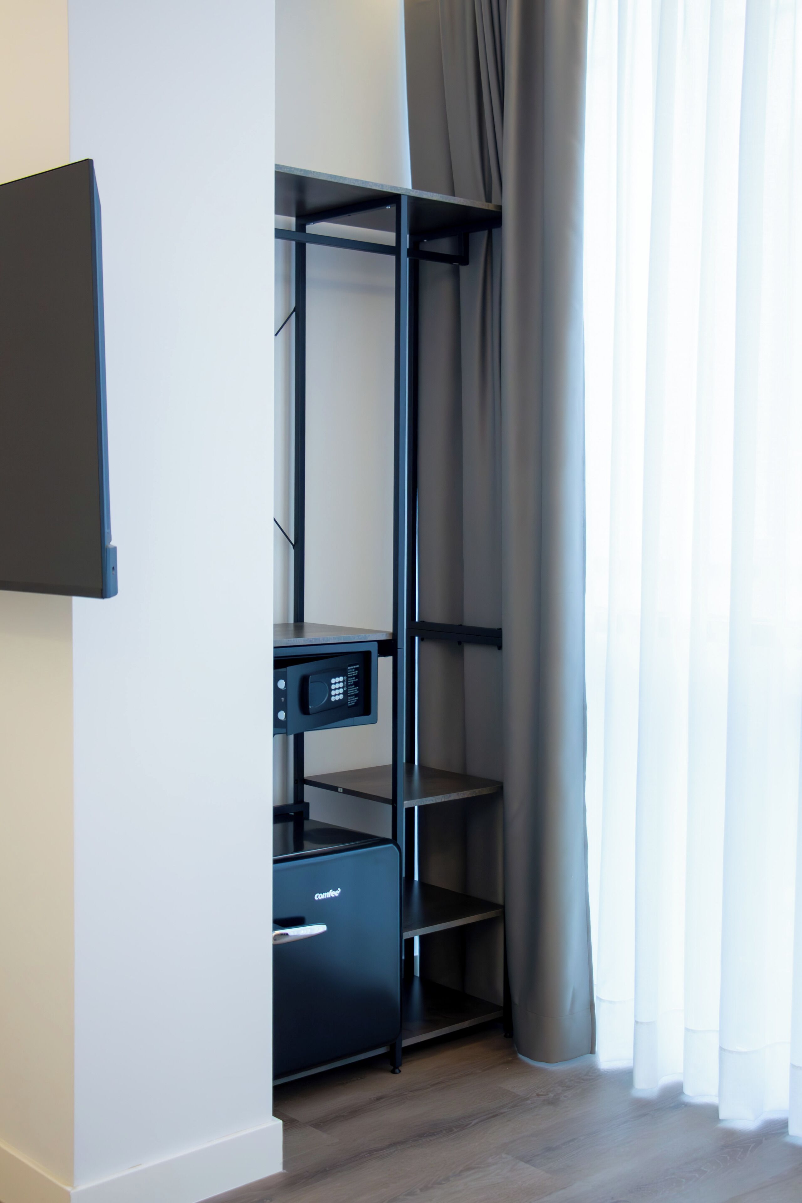Un mueble de almacenamiento compacto con estantes y un pequeño electrodoméstico, probablemente un microondas, en una habitación con piso de madera y cortinas translúcidas.