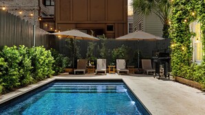 Piscina con sillones de descanso y sombrillas, rodeada de follaje y una valla de madera.