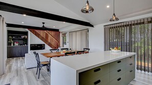 A modern kitchen with a central island, built-in appliances, and a dining area with a view of greenery.