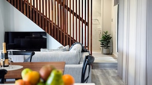 Een moderne woonkamer met een bank, een eettafel met fruit, een televisie en een houten trap.