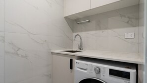 A compact laundry area with a washing machine, a sink, and a marble-tiled wall.