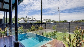 Une piscine dotée d’une terrasse en bois, entourée de plantes tropicales et délimitée par une clôture en métal.