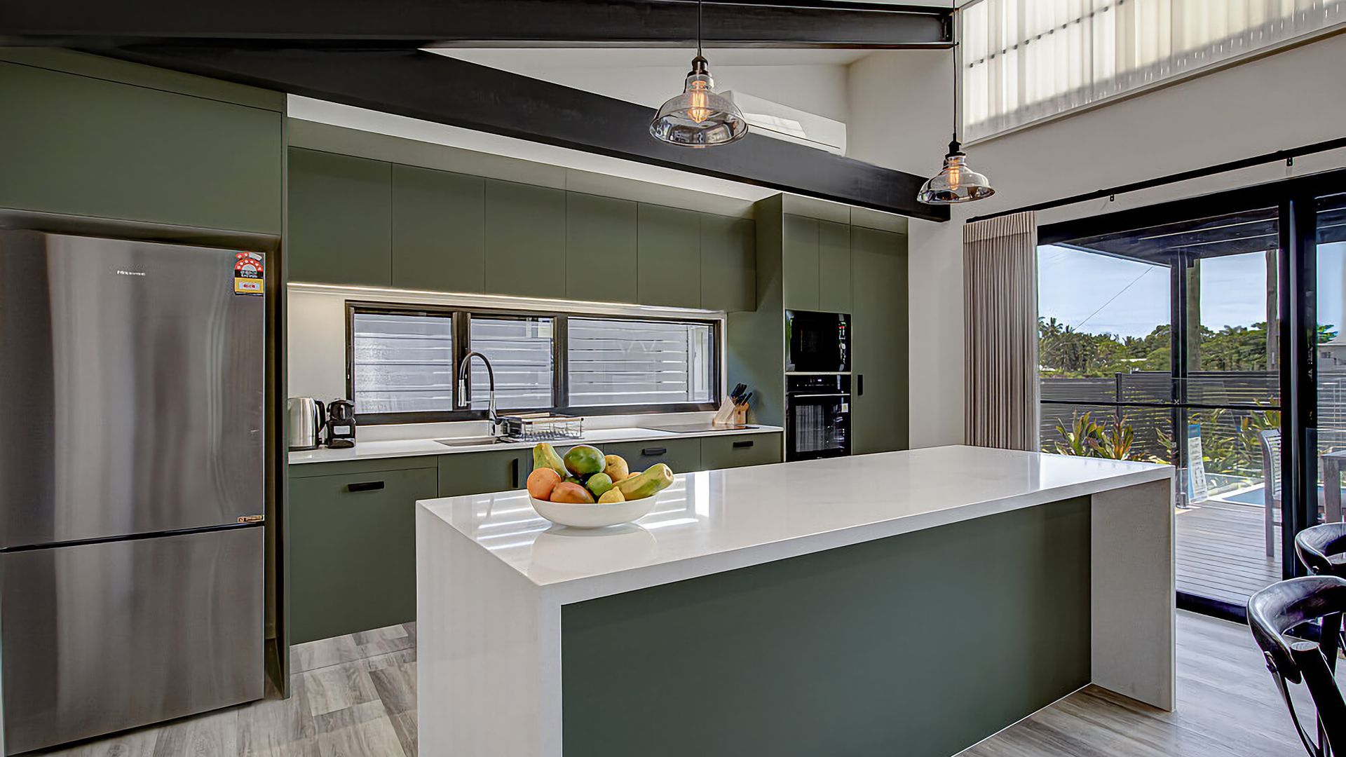 A modern kitchen with a central island, stainless steel appliances, and a large window providing a view of the outdoors.