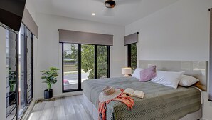 Une chambre moderne avec un grand lit, une table de chevet, une lampe et une vue sur l’extérieur grâce à une porte-fenêtre coulissante.
