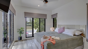 Une chambre moderne avec un grand lit, une table de chevet, une lampe et une vue sur l’extérieur grâce à une porte-fenêtre coulissante.