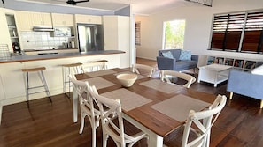 A modern kitchen with white cabinets, a stainless steel refrigerator, and a dining area with a wooden table and white chairs.