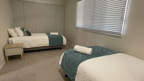 A bedroom with two beds, a nightstand, and a window with blinds.