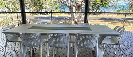 A table with six chairs on an outdoor deck with a view of trees and a body of water.