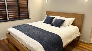 A neatly made bed with a wooden headboard, white bedding, and a dark blue throw blanket.