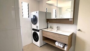 Une petite salle de bain équipée d’un lave-linge, d’un évier et d’un miroir au-dessus du meuble-lavabo.